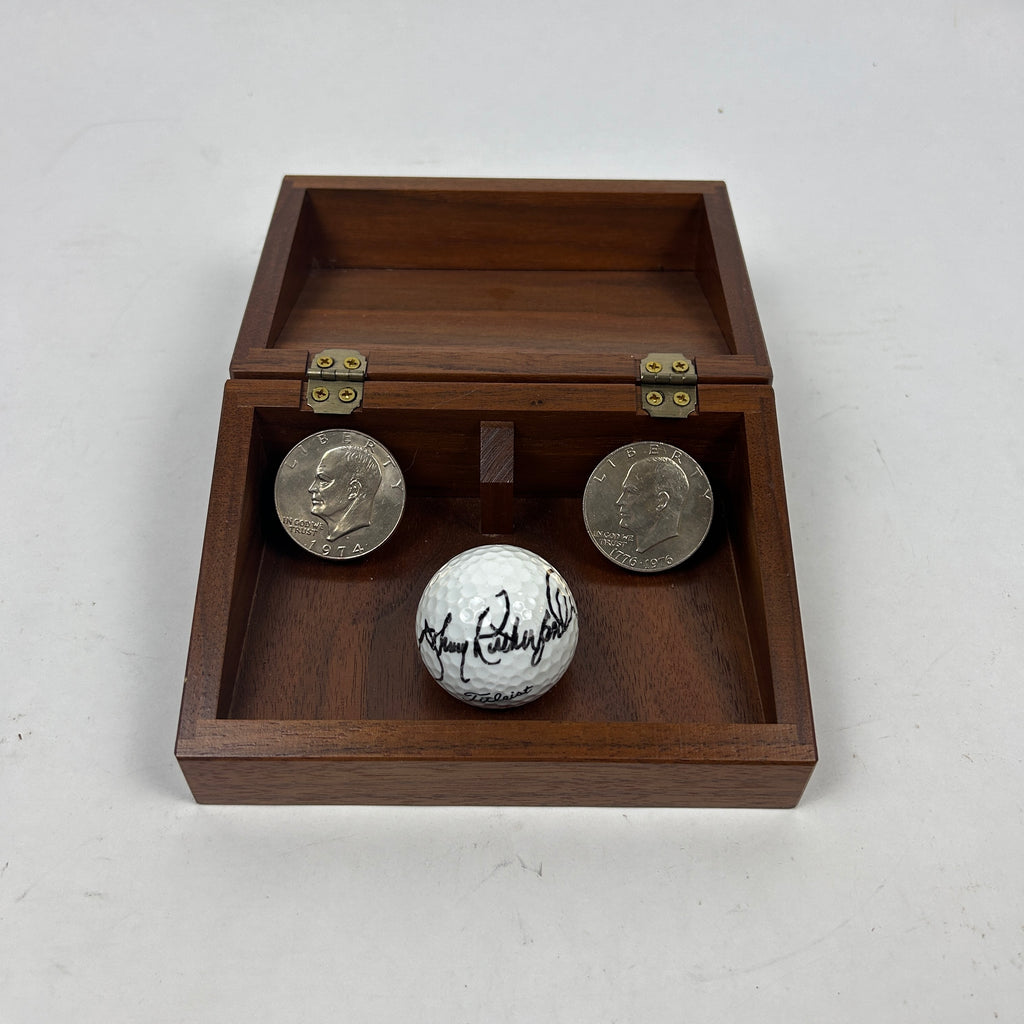 Celebrating Johnny Rutherford's 1974 & 1976 Indianapolis 500 victories is a signed Titleist golf ball and two Eisenhower dollar coins displayed in a wooden hinged box.